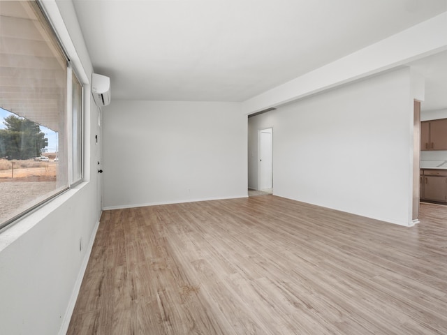 spare room with a wall unit AC, light wood-style floors, and baseboards