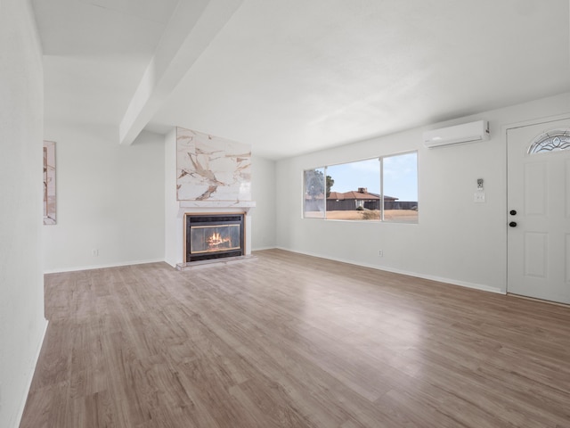 unfurnished living room featuring a premium fireplace, baseboards, wood finished floors, and a wall unit AC