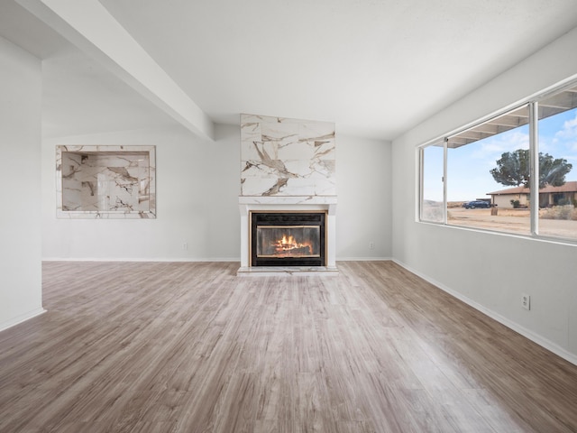 unfurnished living room with beam ceiling, a fireplace, baseboards, and wood finished floors