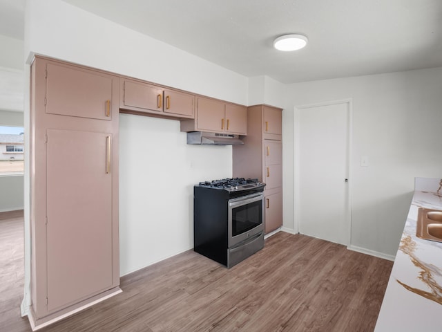 kitchen with under cabinet range hood, stainless steel range with gas cooktop, light countertops, and light wood finished floors