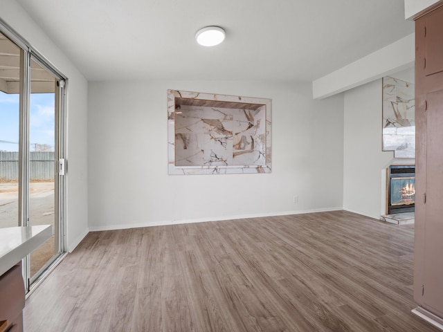 spare room featuring a glass covered fireplace, baseboards, and wood finished floors