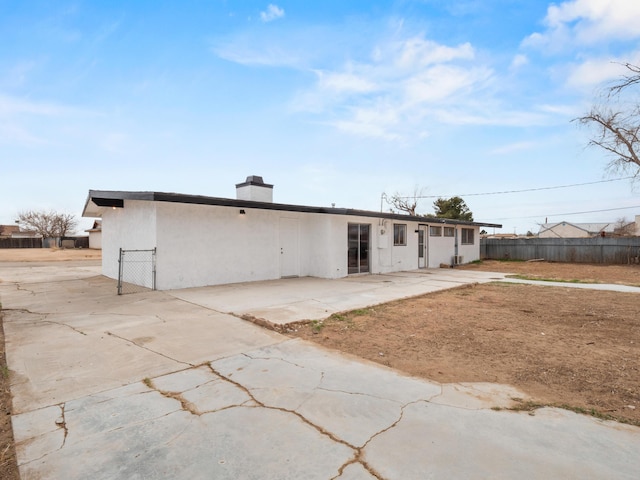 rear view of property featuring stucco siding, a patio, a chimney, and fence