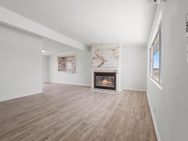 unfurnished living room with light wood-style flooring, lofted ceiling with beams, baseboards, and a premium fireplace