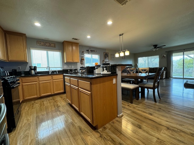 kitchen featuring pendant lighting, sink, black gas stove, a kitchen island, and light wood-type flooring