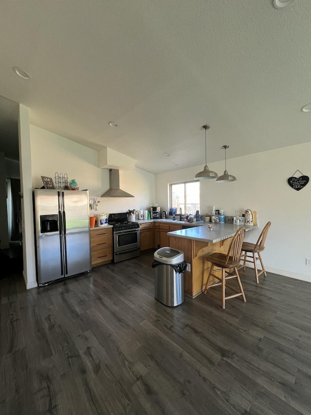 kitchen with kitchen peninsula, appliances with stainless steel finishes, a kitchen bar, wall chimney exhaust hood, and pendant lighting