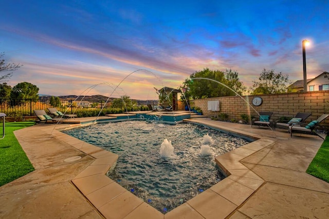 pool at dusk with pool water feature and a patio