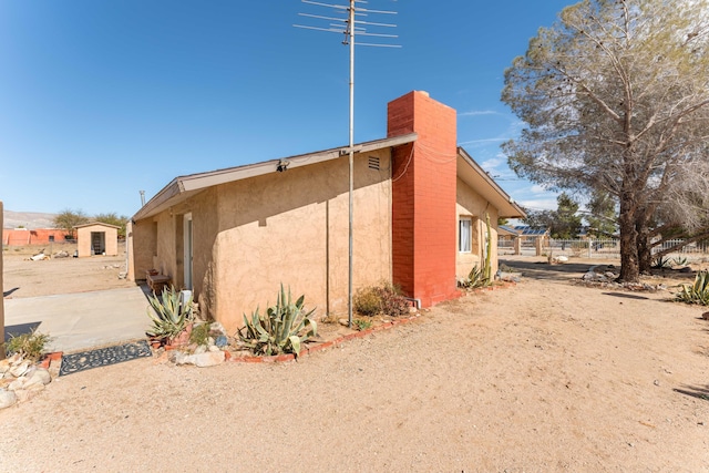 view of home's exterior with a chimney, fence, and stucco siding