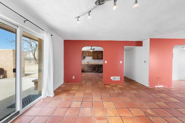 empty room with arched walkways, light tile patterned floors, a textured ceiling, visible vents, and a ceiling fan