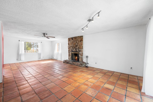 unfurnished living room with a textured ceiling, a stone fireplace, a ceiling fan, and tile patterned floors