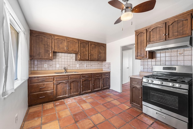 kitchen with under cabinet range hood, a sink, light countertops, stainless steel gas range, and backsplash