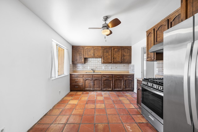 kitchen featuring tasteful backsplash, stainless steel appliances, light countertops, under cabinet range hood, and a sink