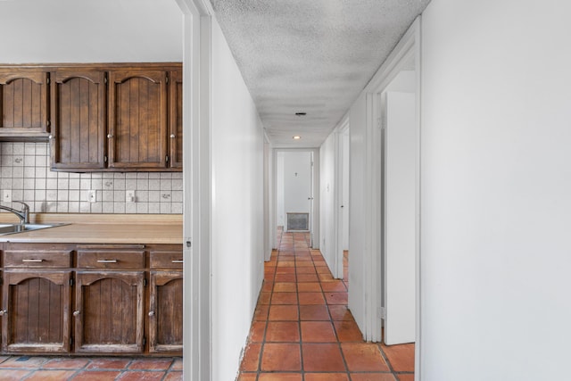 corridor with a sink, visible vents, a textured ceiling, and dark tile patterned flooring