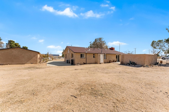 rear view of property with a chimney and stucco siding