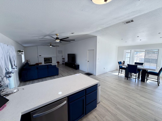 kitchen featuring lofted ceiling, visible vents, dishwasher, light wood finished floors, and a glass covered fireplace