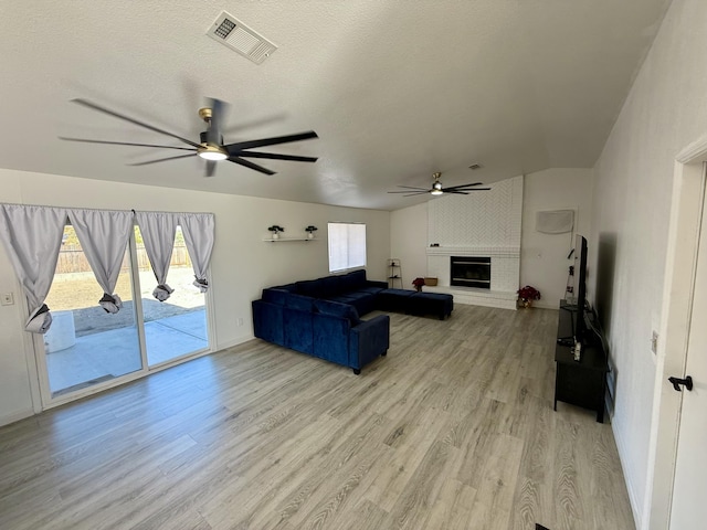 living area with a textured ceiling, light wood-style flooring, visible vents, a ceiling fan, and a brick fireplace