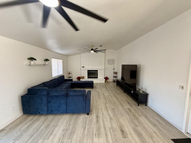 living area with a ceiling fan, a brick fireplace, vaulted ceiling, and light wood-style flooring