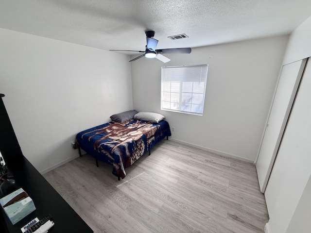 bedroom with light wood finished floors, baseboards, visible vents, and a textured ceiling