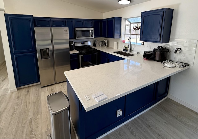 kitchen featuring stainless steel appliances, a peninsula, a sink, blue cabinetry, and light wood finished floors