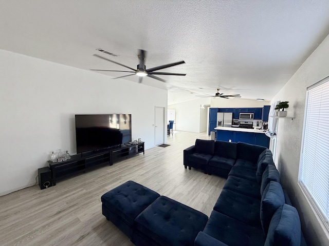 living room featuring lofted ceiling, visible vents, light wood-style flooring, and a textured ceiling