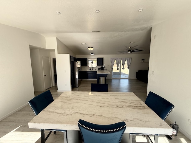 dining room featuring visible vents, baseboards, vaulted ceiling, a ceiling fan, and light wood-style floors