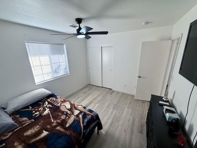 bedroom with visible vents, light wood-style flooring, ceiling fan, a textured ceiling, and a closet