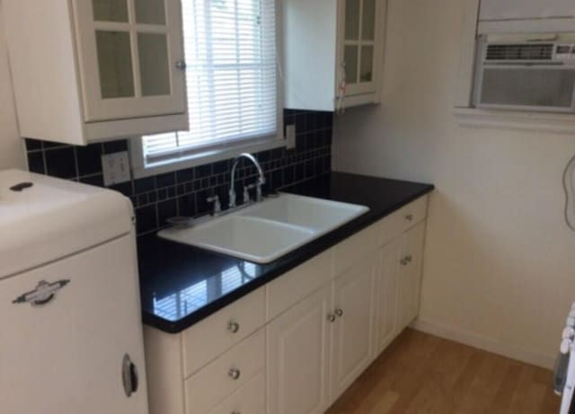 kitchen with light wood finished floors, decorative backsplash, glass insert cabinets, white cabinetry, and a sink