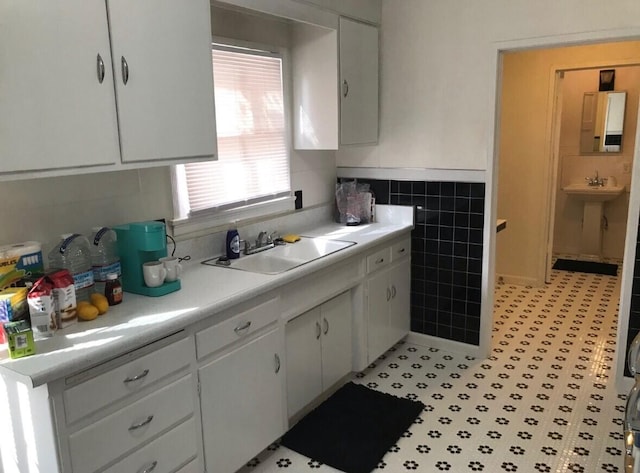 kitchen featuring light countertops, a sink, white cabinetry, and tile walls