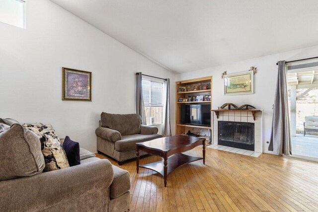 living room featuring built in features, light wood-style flooring, vaulted ceiling, and a fireplace