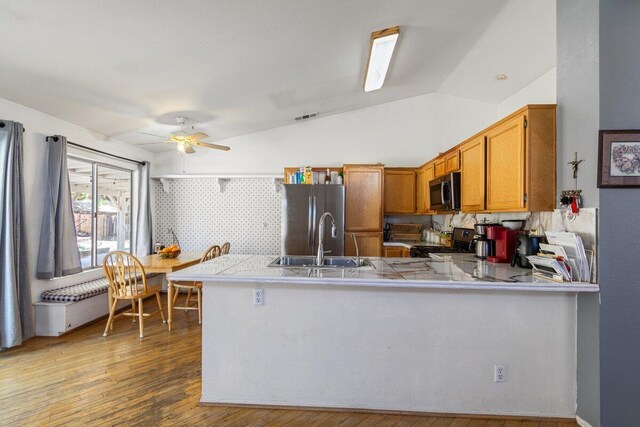 kitchen featuring appliances with stainless steel finishes, a sink, brown cabinetry, a peninsula, and visible vents