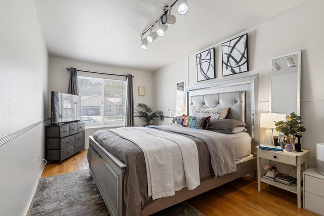 bedroom with rail lighting and wood finished floors
