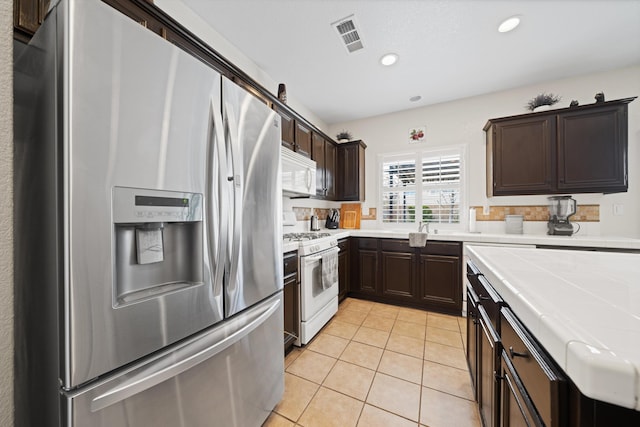 kitchen with white appliances, dark brown cabinets, tile countertops, and light tile patterned flooring