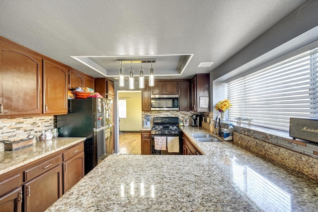 kitchen featuring sink, hanging light fixtures, a tray ceiling, and gas range oven