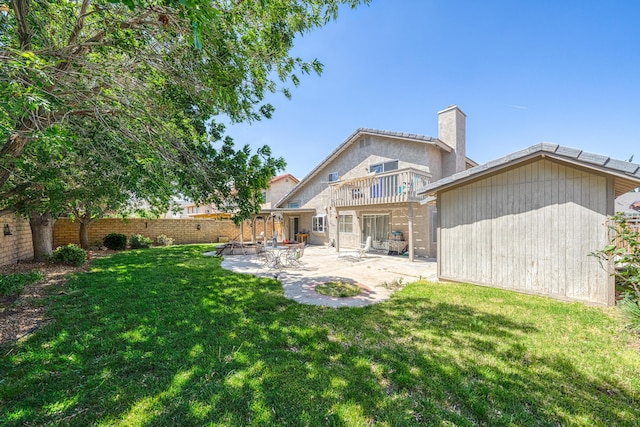 rear view of house with a fenced backyard, a chimney, a balcony, a lawn, and a patio