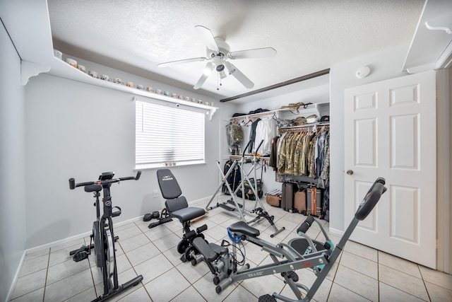 exercise area with baseboards, a ceiling fan, a textured ceiling, and light tile patterned floors