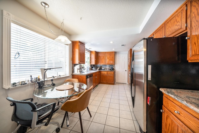 kitchen with brown cabinetry, a textured ceiling, a sink, light tile patterned floors, and stainless steel appliances