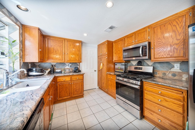kitchen featuring visible vents, brown cabinetry, tasteful backsplash, a sink, and appliances with stainless steel finishes