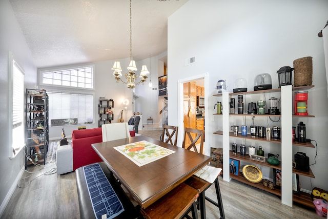 dining space with an inviting chandelier, wood finished floors, visible vents, and high vaulted ceiling