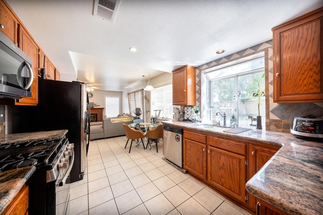 kitchen featuring brown cabinetry, visible vents, appliances with stainless steel finishes, open floor plan, and light tile patterned flooring