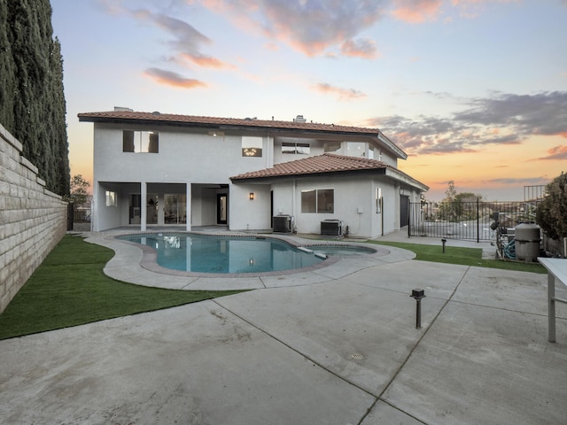 back house at dusk featuring a pool with hot tub, cooling unit, and a patio area