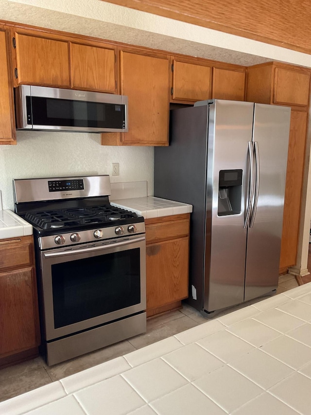 kitchen with tile counters, light tile patterned floors, and appliances with stainless steel finishes