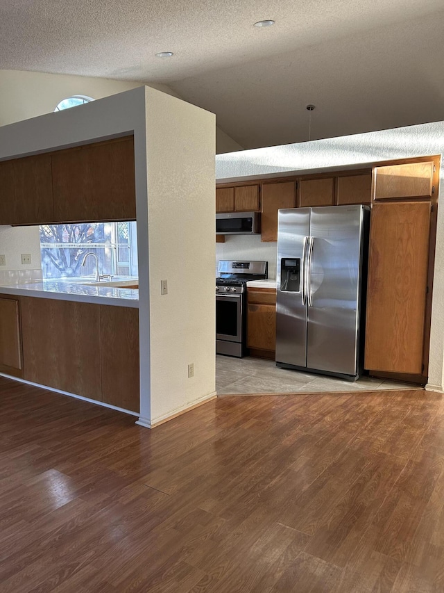 kitchen featuring hardwood / wood-style floors, lofted ceiling, stainless steel appliances, and a textured ceiling