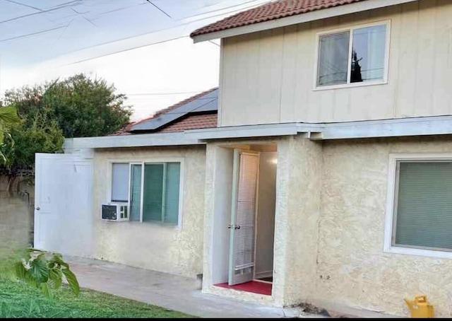 view of side of property with a tiled roof, stucco siding, cooling unit, and roof mounted solar panels