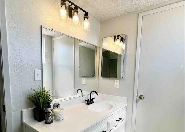 bathroom featuring a textured ceiling, a textured wall, and vanity