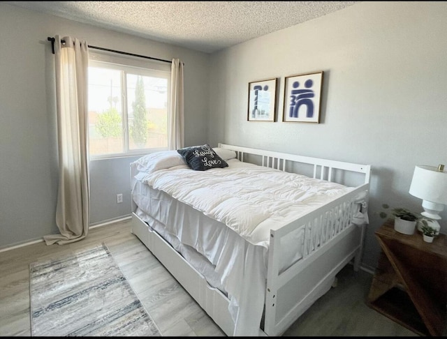 bedroom with light wood-style floors, baseboards, and a textured ceiling