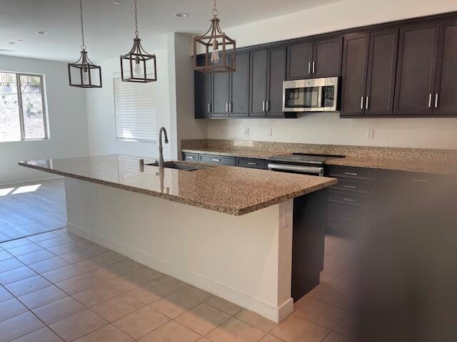 kitchen featuring light stone counters, dark brown cabinetry, stainless steel appliances, a kitchen island with sink, and sink