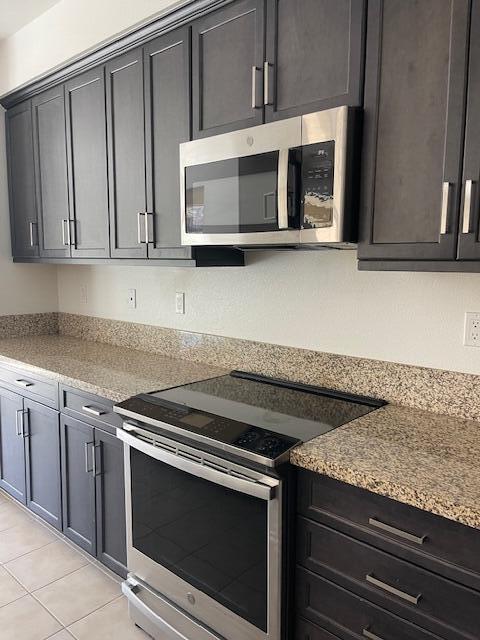 kitchen with light stone countertops, light tile patterned flooring, and stainless steel appliances