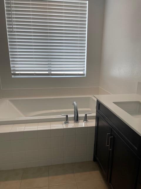 bathroom featuring tile patterned floors, vanity, and a relaxing tiled tub