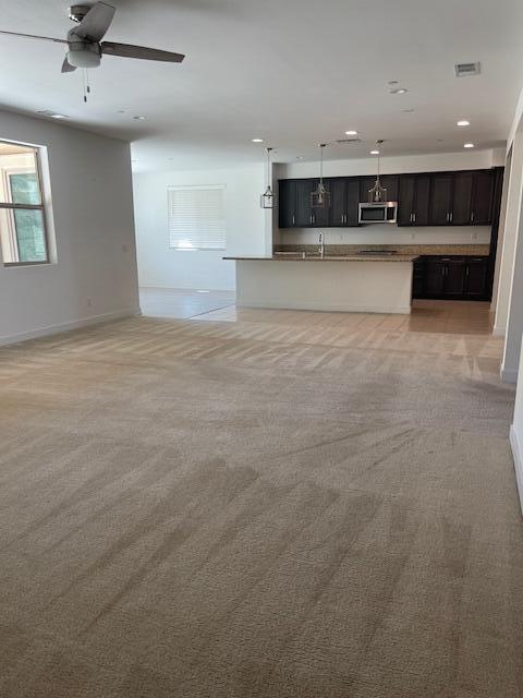 unfurnished living room featuring ceiling fan, light colored carpet, and sink