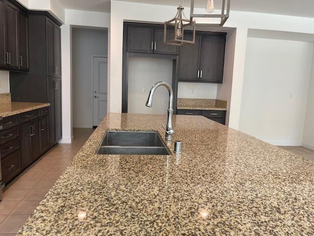 kitchen featuring dark brown cabinets, light stone counters, sink, and an island with sink