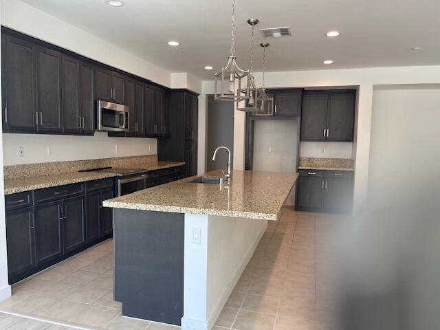 kitchen with sink, an island with sink, light tile patterned flooring, light stone counters, and stainless steel appliances